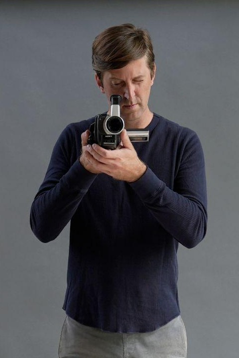 Tomasz Werner holding a camcorder against a grey backdrop